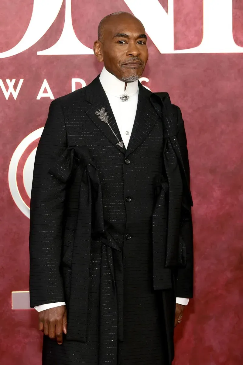 نجم يرتدي بدلة سوداء أنيقة مع تفاصيل فنية، يظهر في حفل توزيع جوائز توني 78، محاطًا بأجواء احتفالية مميزة.