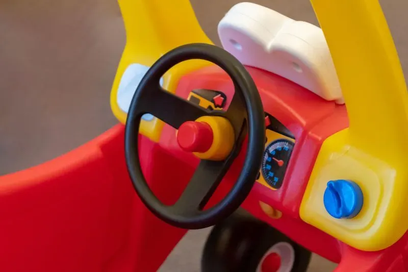 عجلة قيادة لعبة أطفال ملونة باللونين الأحمر والأصفر، مع أزرار تحكم وأدوات قياس، تعكس تأثير التعريفات الجمركية على صناعة الألعاب.