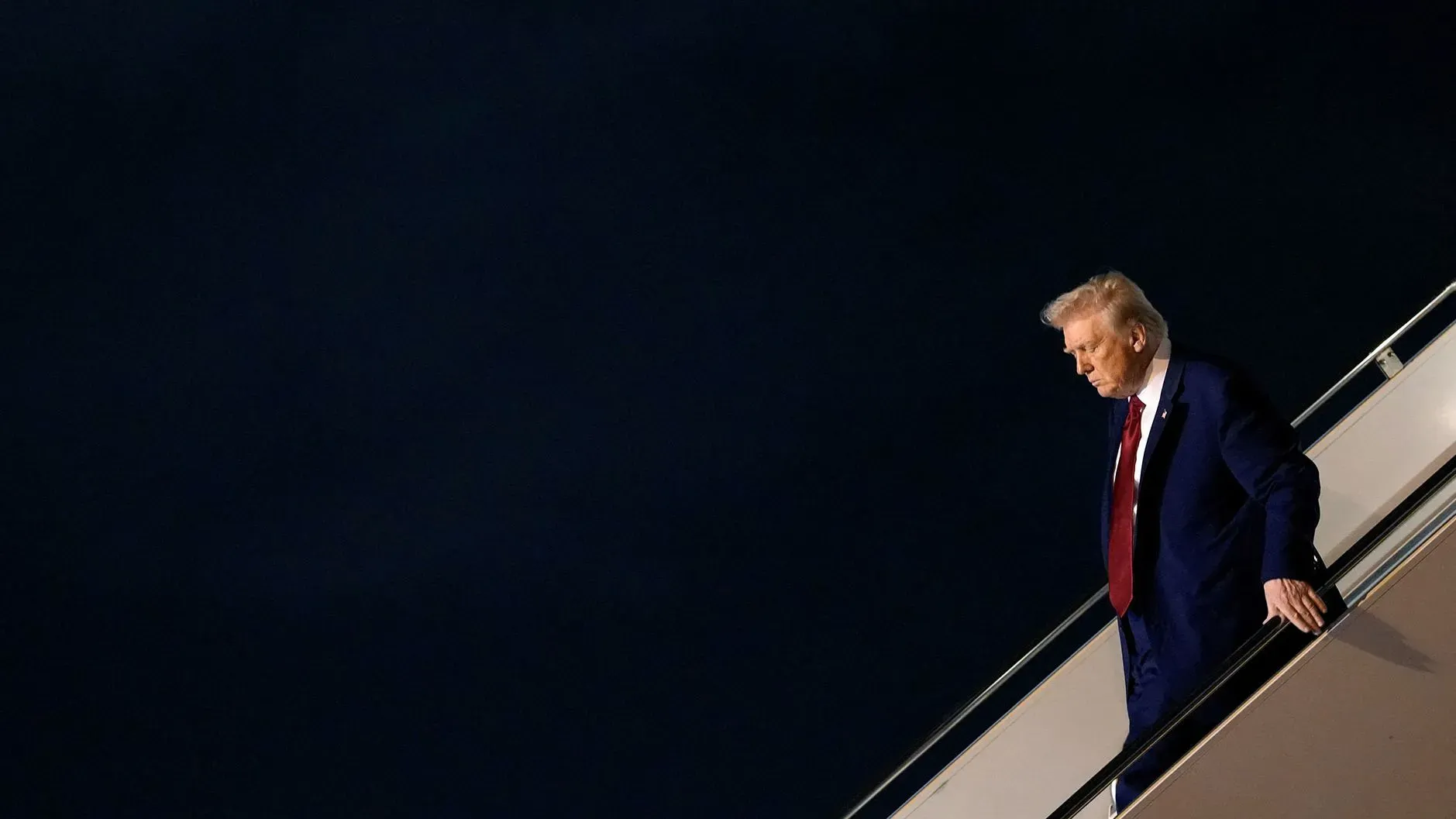 رجل يرتدي بدلة زرقاء ينزل من سلم طائرة في مشهد يعكس التوتر السياسي حول سياسات التعليم والتنوع.