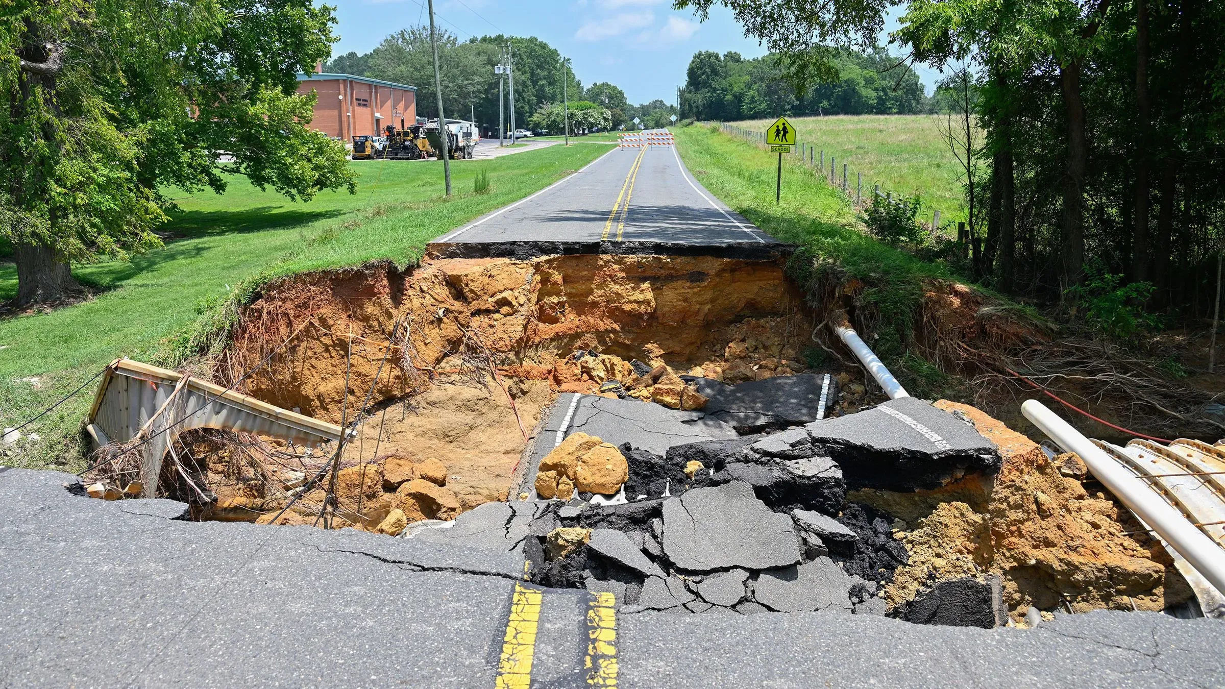 تصور لشارع متضرر نتيجة انهيار أرضي، حيث انقسمت الأسفلت وكُشف عن التربة تحتها، مما يبرز آثار الكوارث الطبيعية.