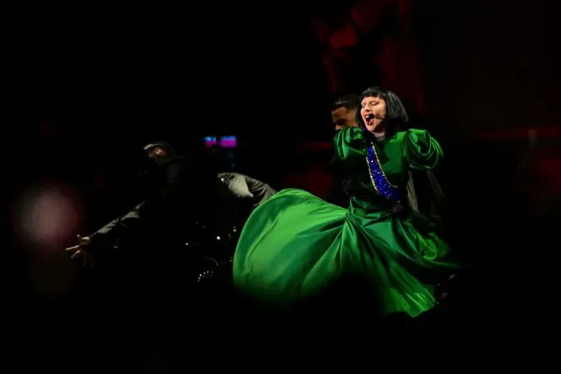 ليدي غاغا تؤدي عرضًا حيويًا في ريو دي جانيرو، مرتدية فستانًا أخضر، محاطة بالراقصين، خلال حفلة مجانية على شاطئ كوباكابانا.