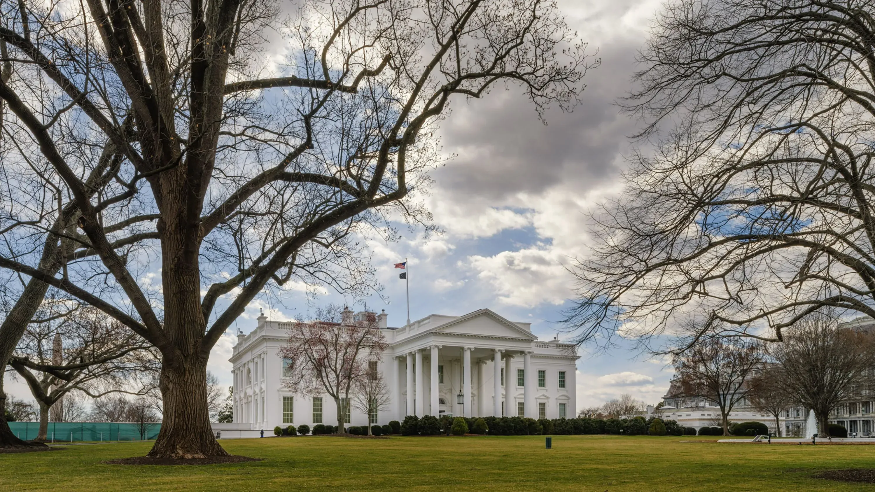 البيت الأبيض محاط بأشجار عارية تحت سماء غائمة، مما يعكس الأجواء السياسية المتوترة حول قضايا التمويل الصحي.