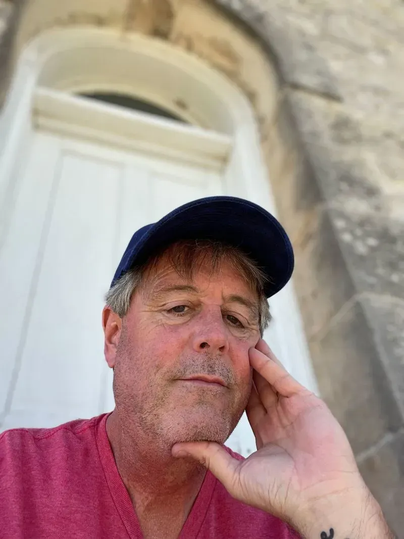 رجل يجلس على الدرج أمام باب قديم، يعبر عن مشاعر التفكير والقلق، في سياق مناقشة حول العنف المنزلي وتأثيره على الرجال.