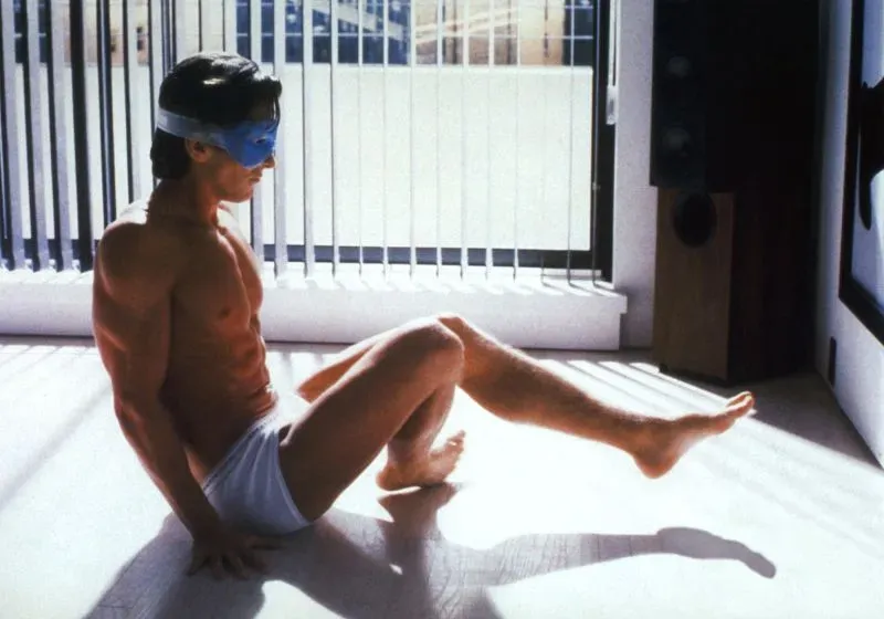 رجل يرتدي قناعًا للعين ويقوم بتمارين رياضية في شقته، يعكس روتين العناية بالبشرة المفرط في الثقافة الاستهلاكية.