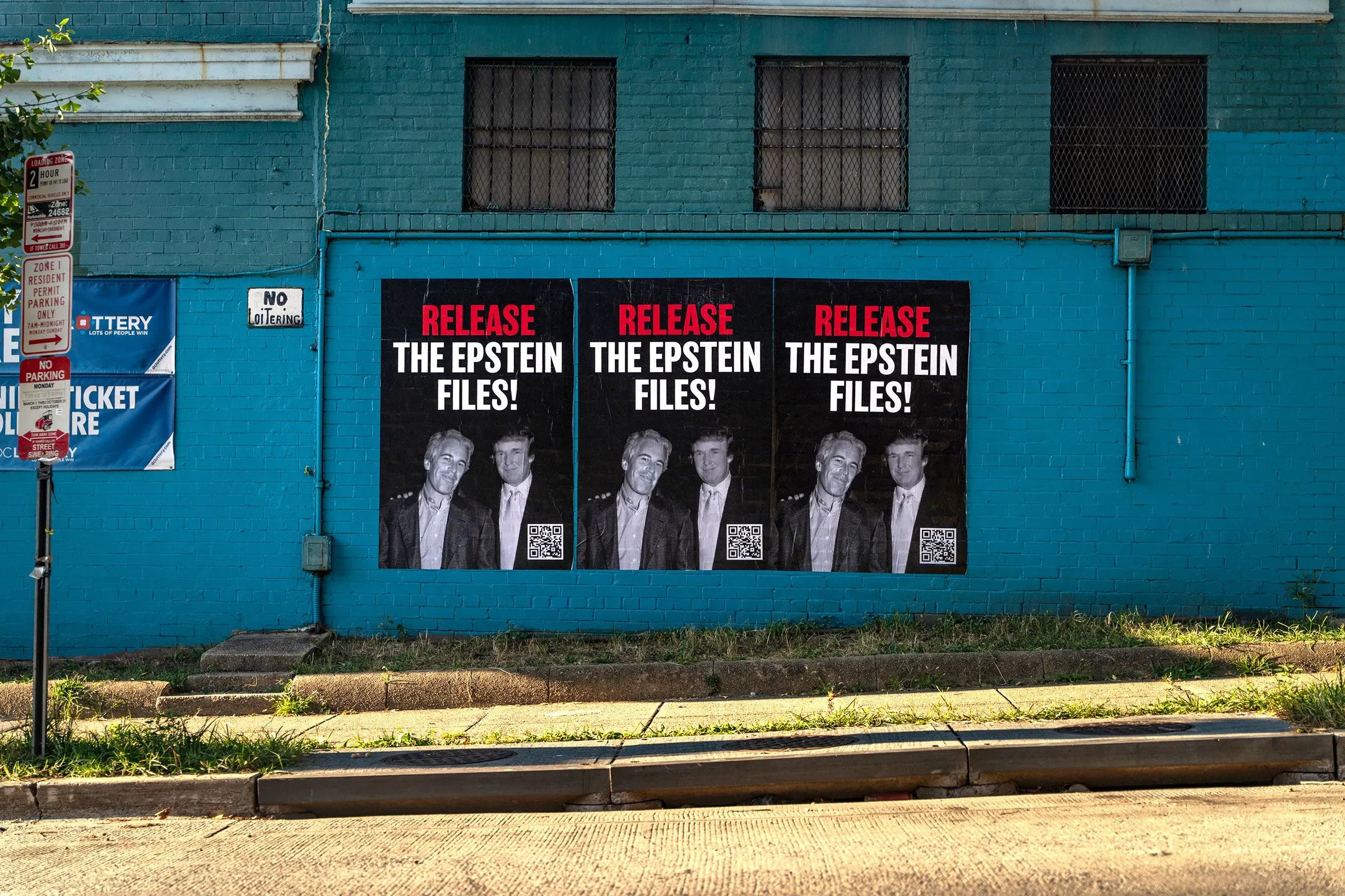 ملصقات على جدار أزرق تطالب بإصدار ملفات إبشتاين، تظهر صوراً لرجلين معاً، مما يثير تساؤلات حول علاقتهما.