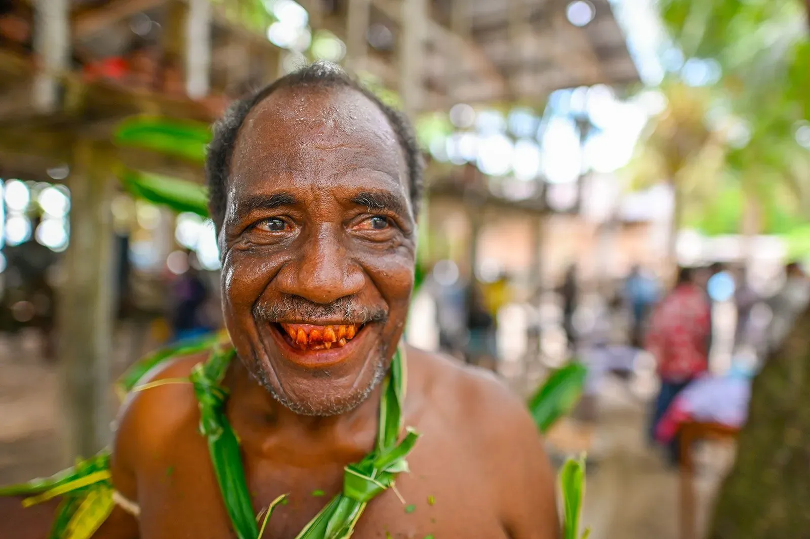 رجل مبتسم يظهر آثار جوز التنبول على أسنانه، محاط بأجواء طبيعية، مما يعكس تقليد مضغ جوز التنبول في المجتمعات القديمة.