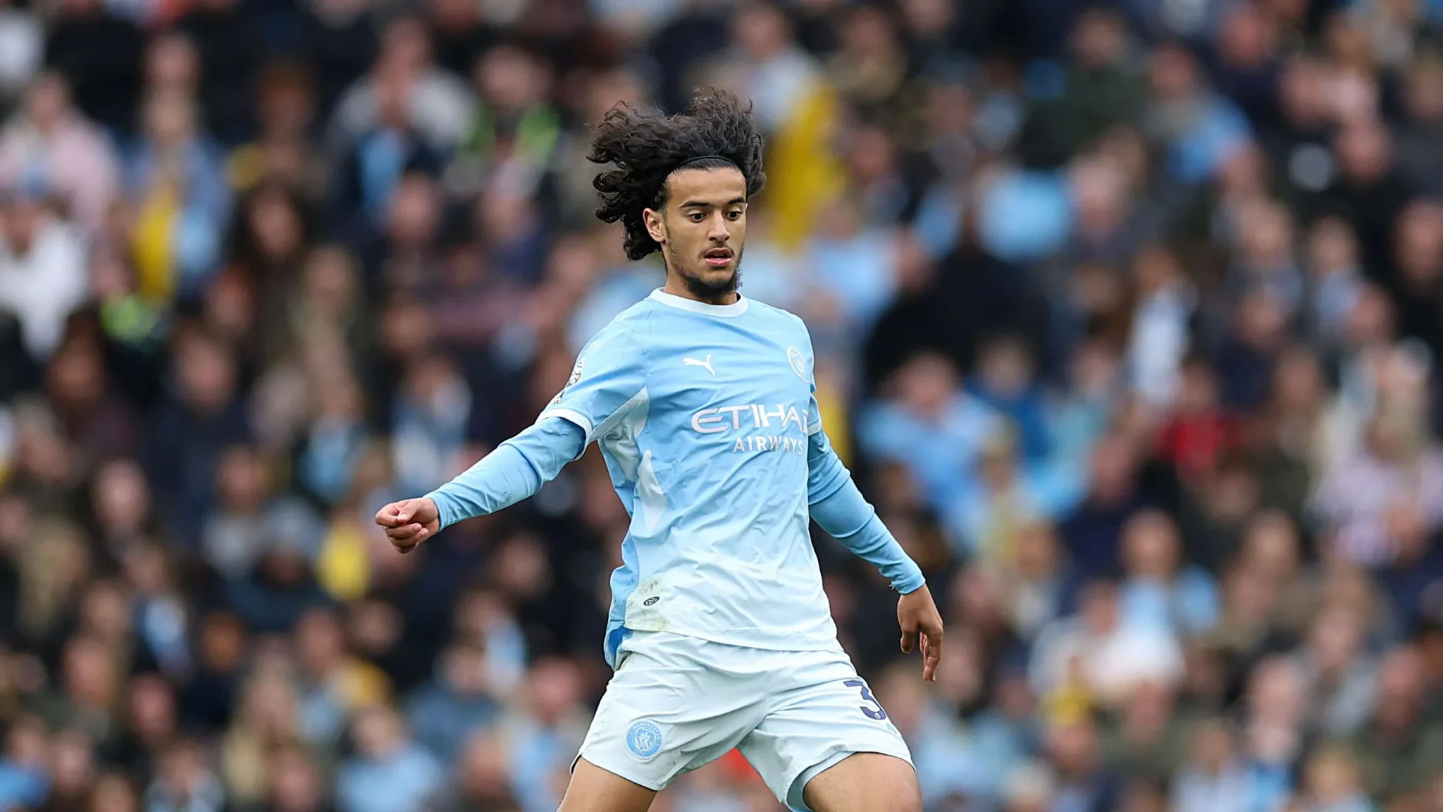 أيوب بوعدي لاعب وسط مانشستر سيتي يرتدي الزي الأزرق أثناء مباراة الدوري الإنجليزي، يعكس دوره الدفاعي والتمريرات الدقيقة.