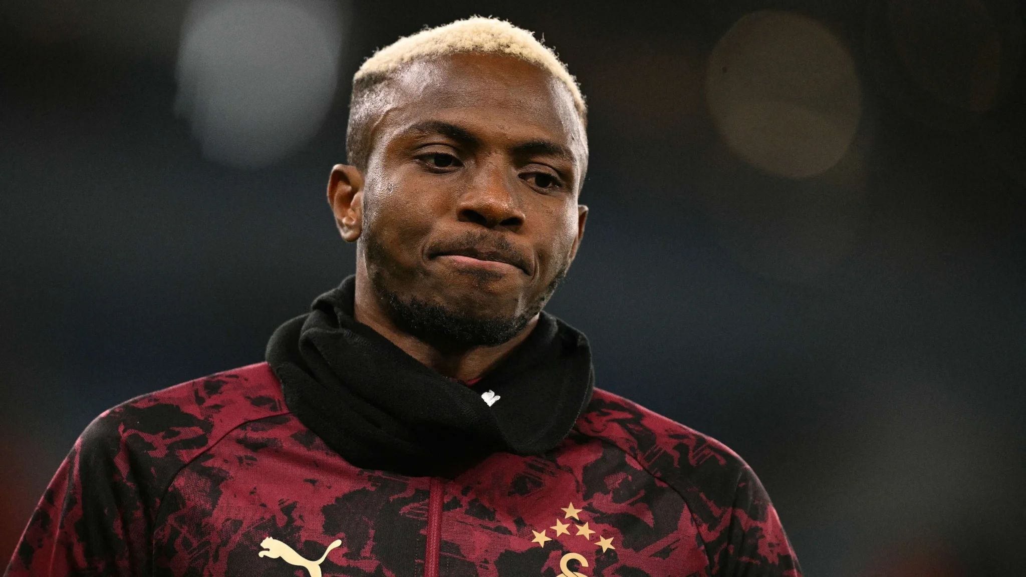 لاعب فيكتور أوسيمين مهاجم جالاتا سراي يرتدي زي تدريب أحمر وأسود مع وشاح أسود، مرشح محتمل لبرشلونة حسب تحليل الذكاء الاصطناعي.