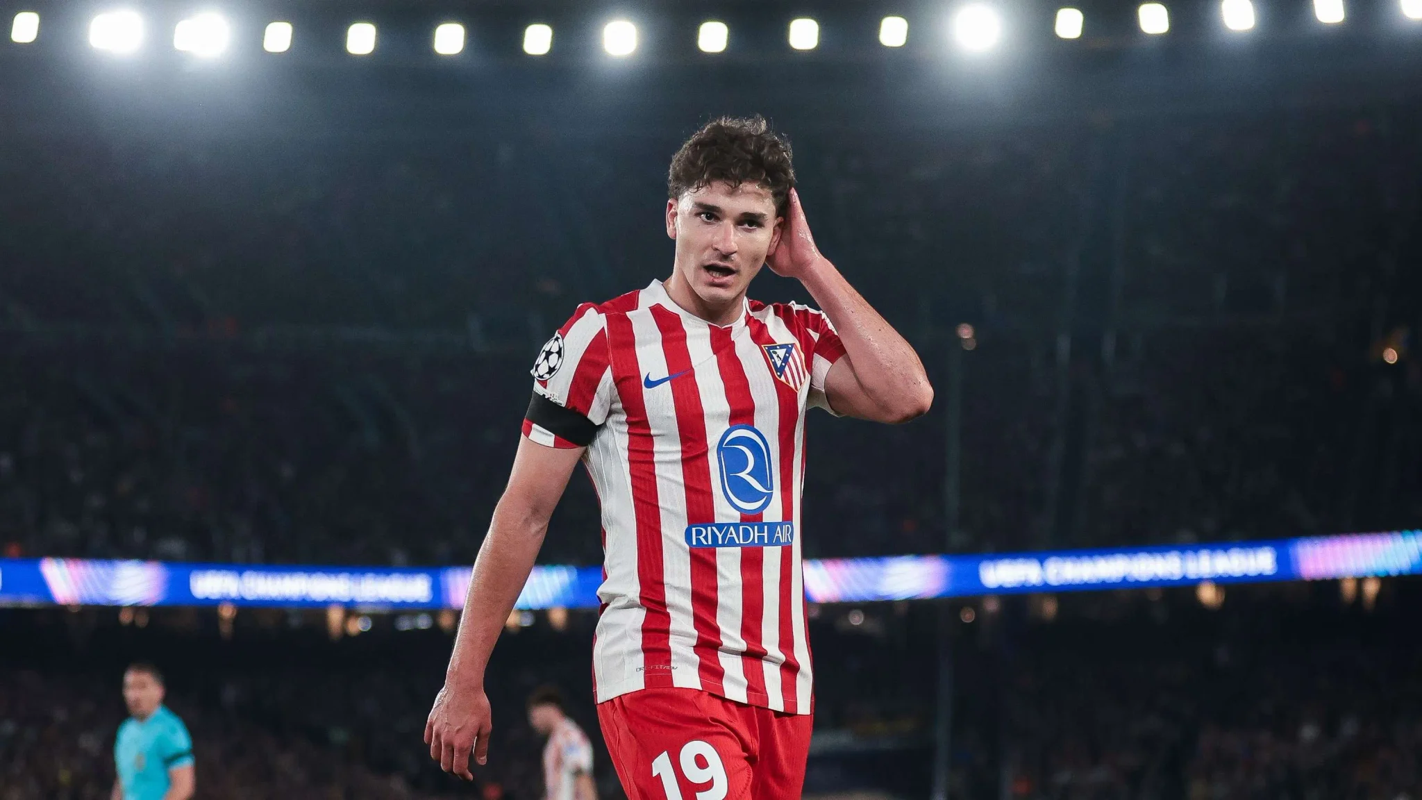 جوليان ألفاريز لاعب أتلتيكو مدريد يرتدي زي الفريق الأحمر والأبيض خلال مباراة في دوري أبطال أوروبا، مع تركيز على وجهه وتعابير الحيرة أو التفكير.