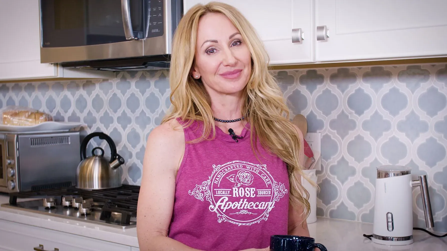 امرأة مبتسمة ترتدي قميصًا رياضيًا، تقف في مطبخ عصري، تحمل كوبًا، مما يعكس أهمية الحركة والمرونة في الحياة اليومية.