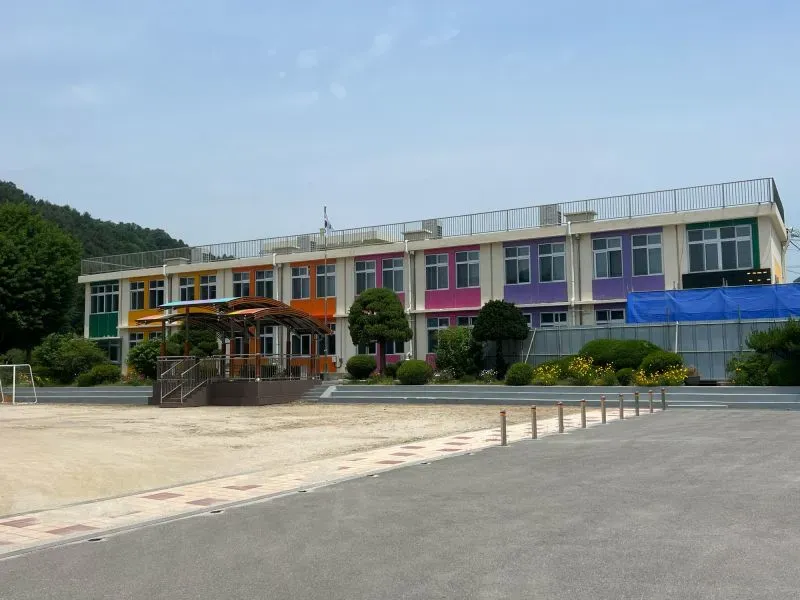 مدرسة حديثة ملونة تقع في منطقة جبلية، محاطة بالأشجار، تمثل مكانًا تعليميًا في كوريا الجنوبية.