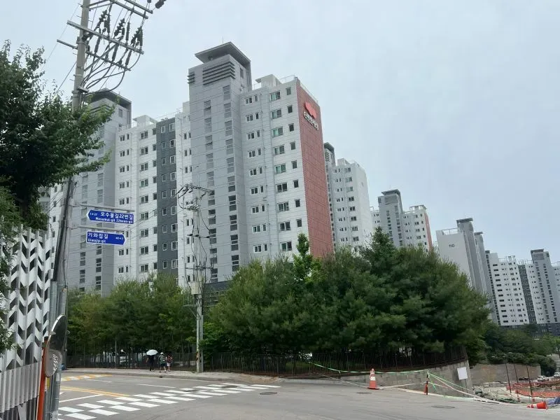 مباني سكنية حديثة تحيط بها أشجار، تعكس التغيير الذي شهدته منطقة دانغنيم، حيث كانت تعيش عائلة مين قبل الحرب الكورية.