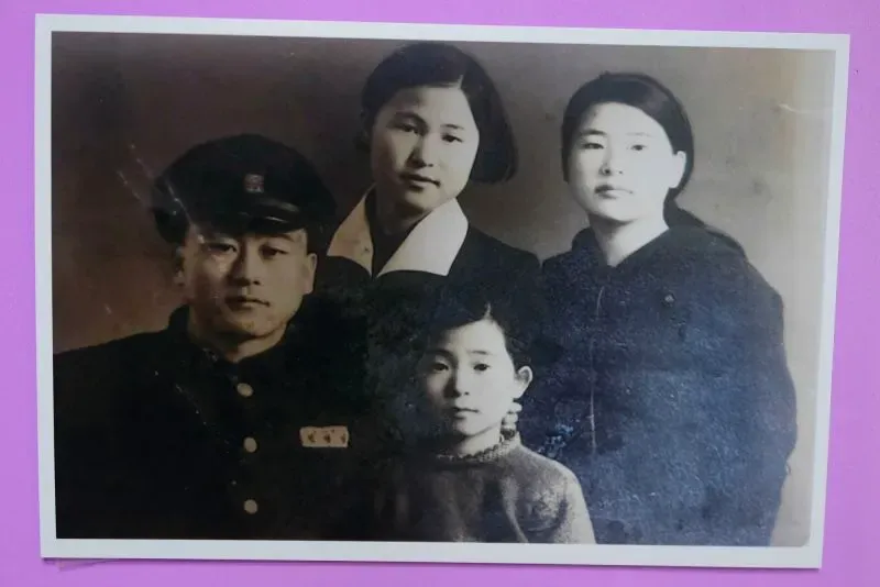 صورة عائلية قديمة تظهر أربعة أفراد، بينهم رجل يرتدي زيًا عسكريًا، ونساء في ملابس عصرية، تعكس ذكريات عائلية مؤلمة خلال الحرب الكورية.