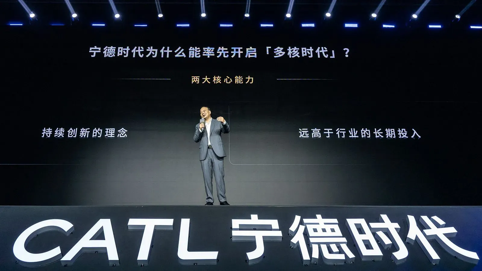 رجل يتحدث على المنصة في حدث لشركة CATL، مع عرض نصوص تتعلق بتكنولوجيا البطاريات الكهربائية وأهداف الشركة المستقبلية.