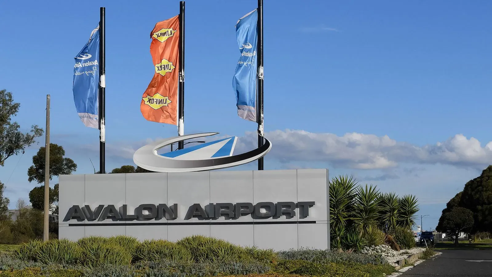 لافتة مطار أفالون في أستراليا، مع أعلام ملونة ترفرف في الهواء، تعكس حالة الطوارئ بعد حادثة تهديد مسلح.
