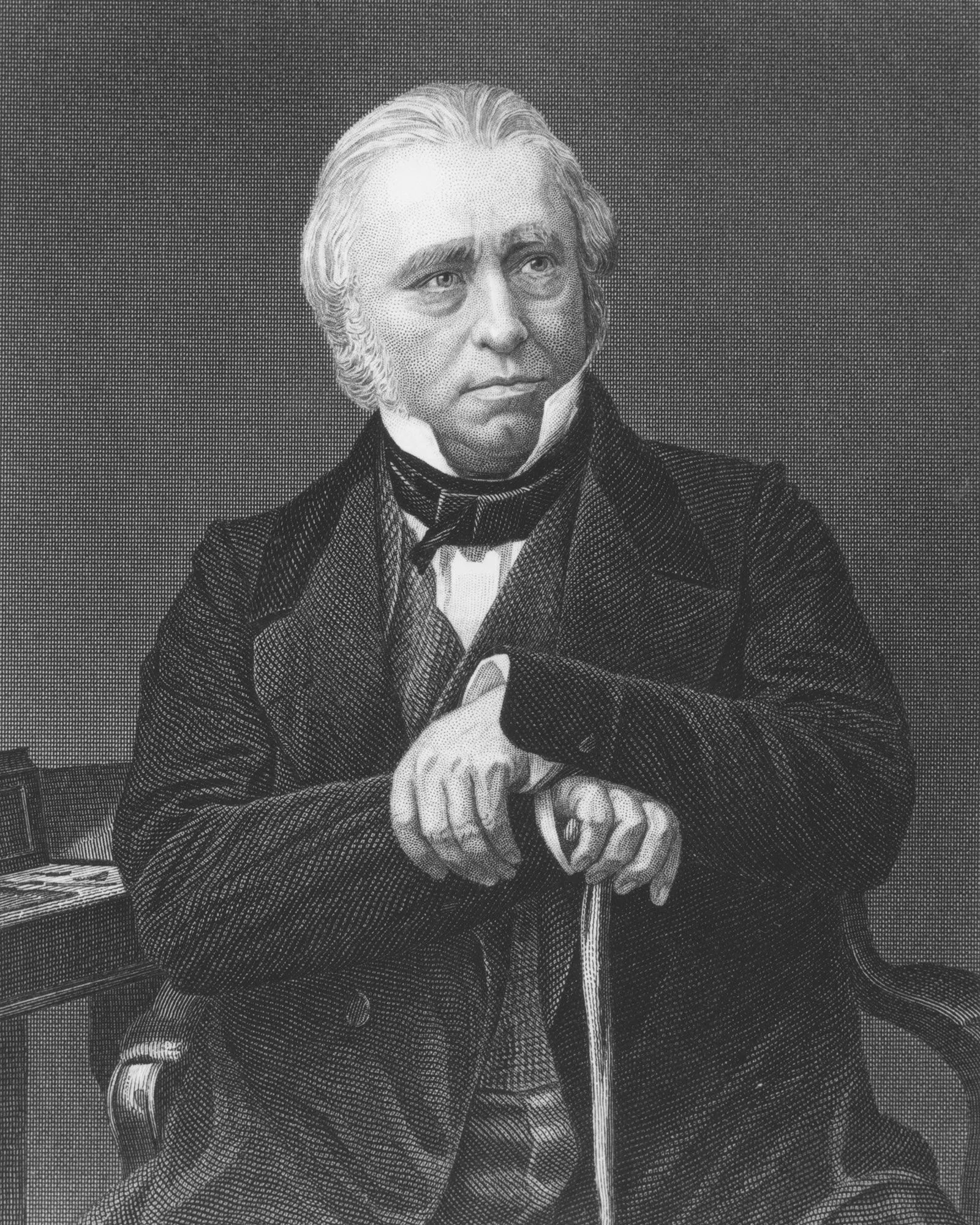 رجل مسن ذو لحية وشعر رمادي، يرتدي بدلة رسمية، يجلس مع عصا في يده، يعكس تأثير الاستعمار البريطاني على الهند.