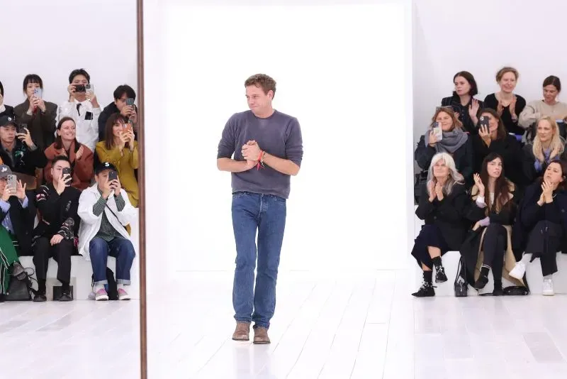 المصمم جوناثان أندرسون يتلقى تصفيق الجمهور بعد عرضه في أسبوع الموضة، مع حشد من الحضور يلتقطون الصور.