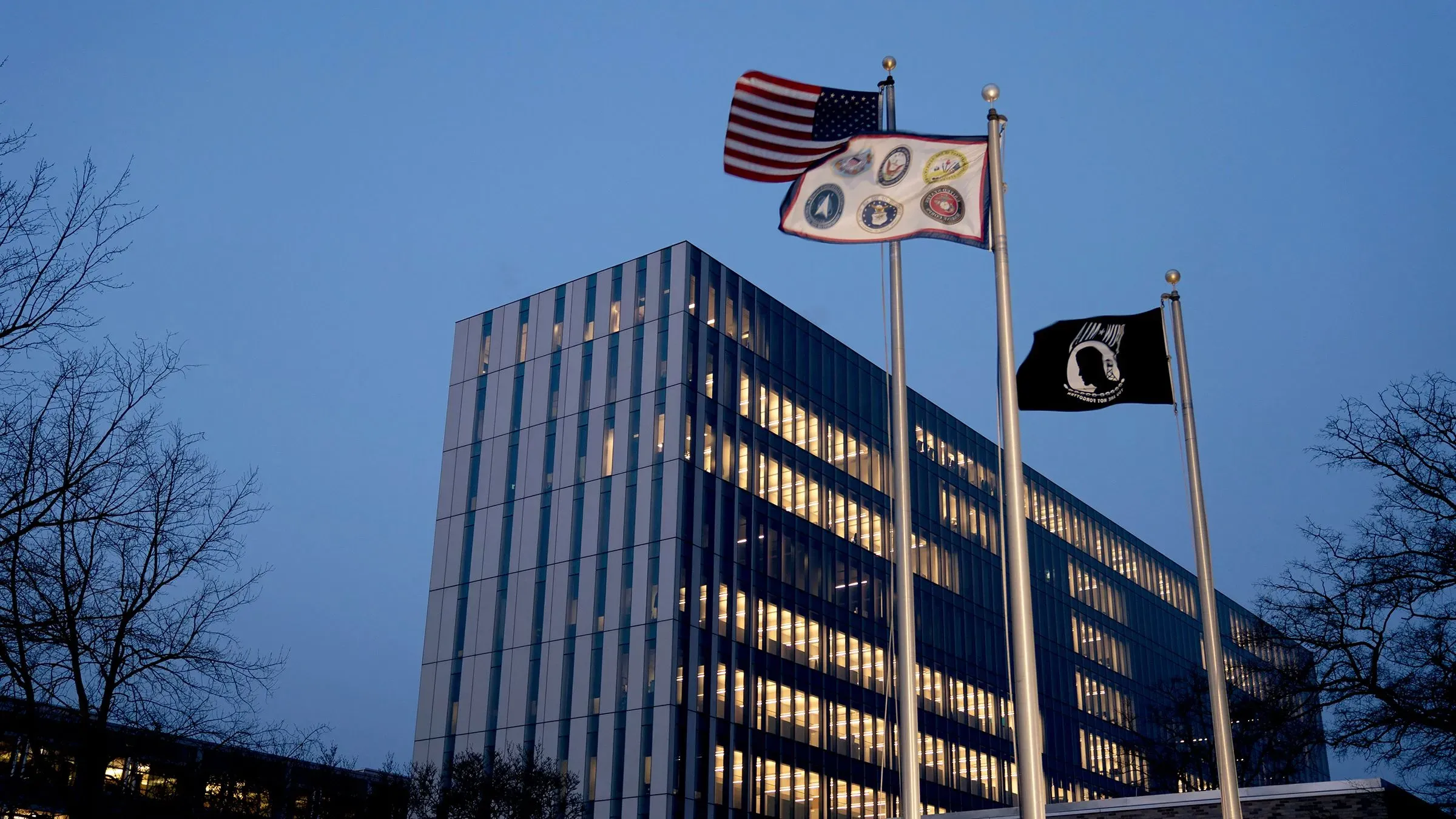 مبنى إدارة الضمان الاجتماعي مع الأعلام الأمريكية وأعلام أخرى، يظهر في المساء مع إضاءة النوافذ، يعكس التغييرات المحتملة في الوكالة.