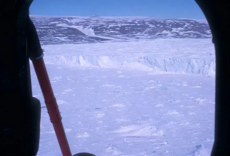 منظر لغطاء جليدي في غرينلاند يظهر الجليد الواسع والجبال خلفه، مع تلميحات عن محطة أبحاث تحت الجليد، مما يعكس تاريخ كامب سينتشري.