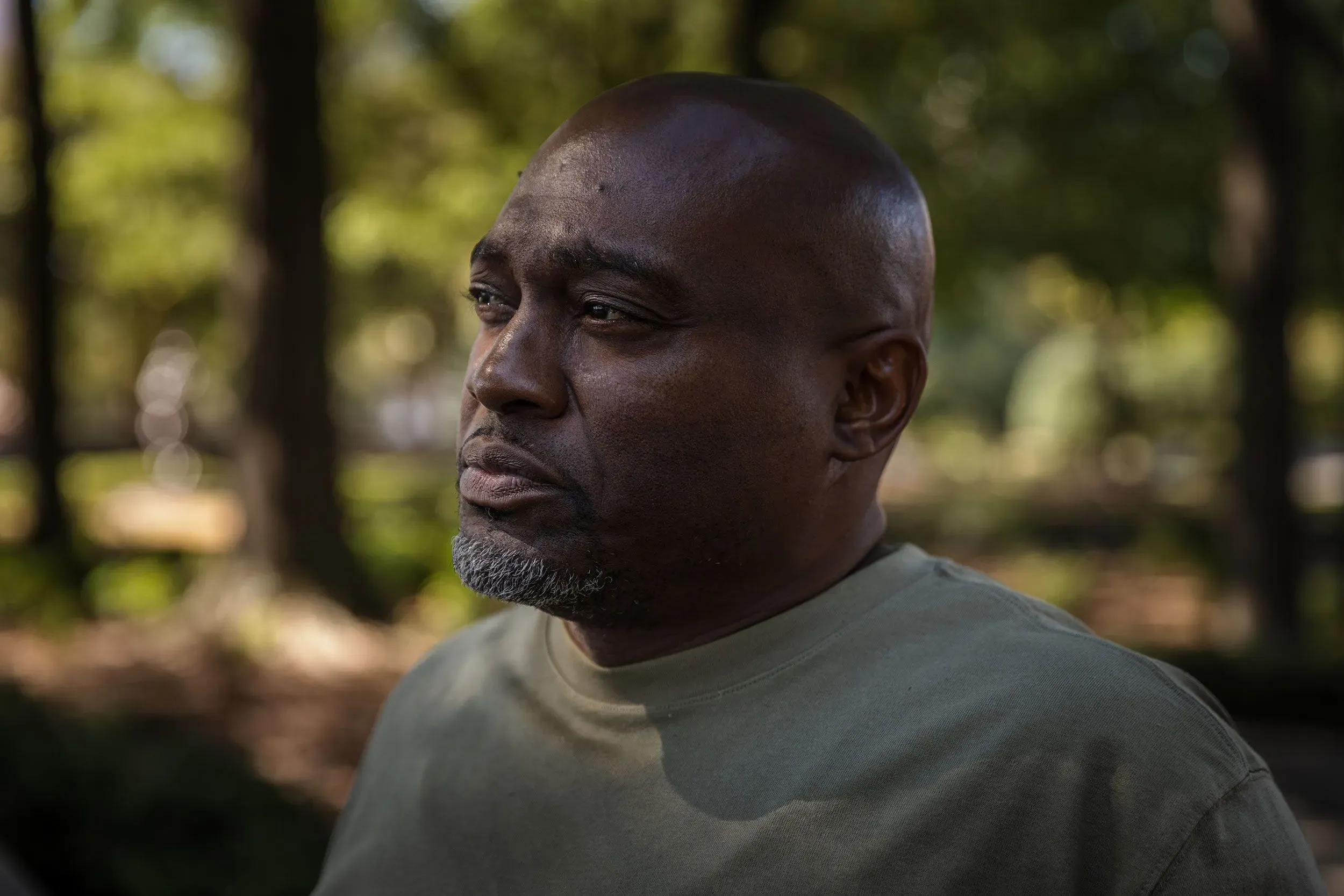 صورة لرجل في منتصف العمر، يبدو عليه التأمل والقلق، محاط بأشجار في حديقة، يعكس معاناة المشردين في أتلانتا.