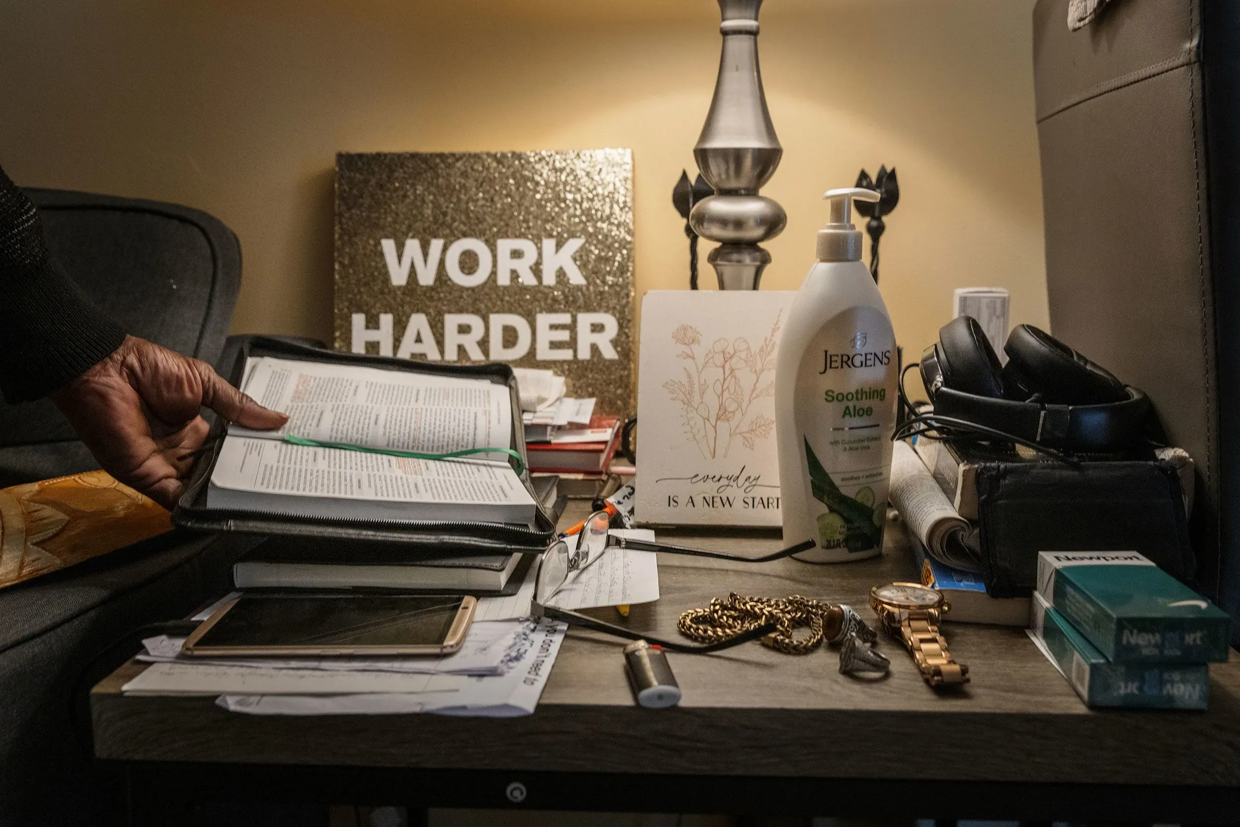 طاولة تحتوي على مجموعة من الأغراض الشخصية، بما في ذلك كتاب مفتوح، زجاجة لوشن، وساعة، مع لافتة مكتوب عليها "اعمل بجد".