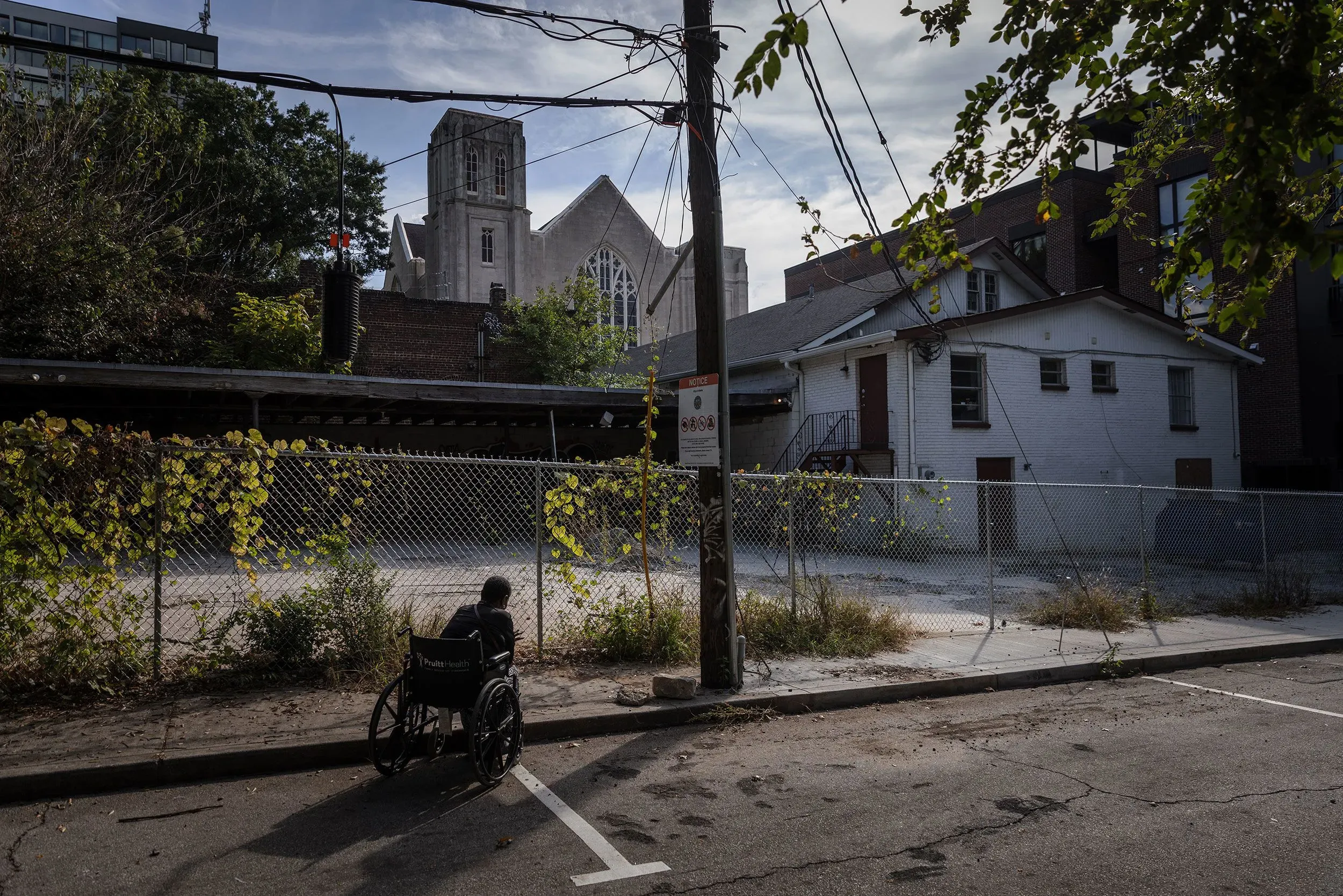 كرسي متحرك في شارع مهجور أمام سياج، مع كنيسة في الخلفية، يعكس مشهد التشرد والتحديات في أتلانتا.