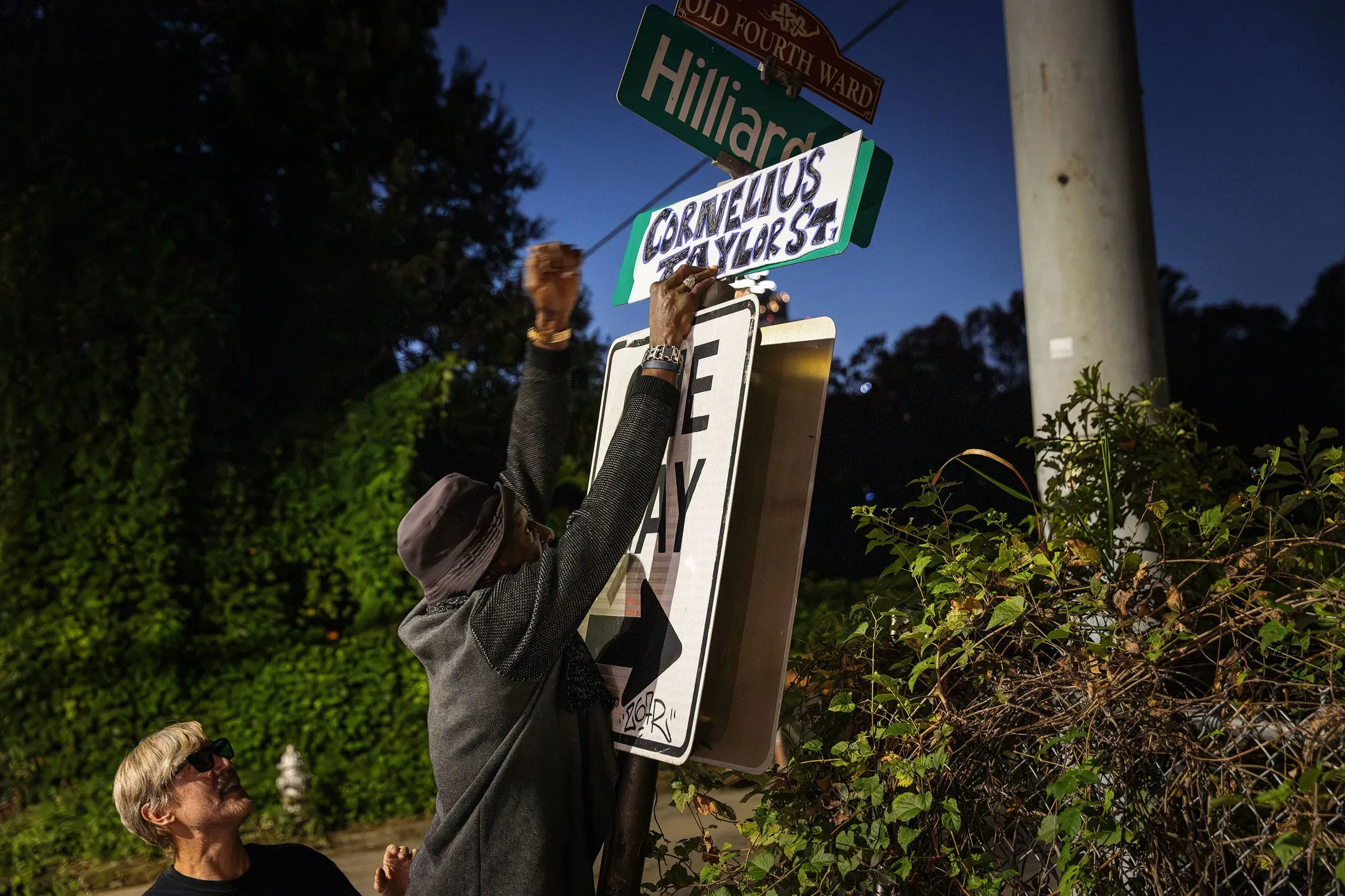 شخصان يعلقان لافتة تحمل اسم "شارع كورنيليوس تايلور" على إشارة مرورية في أتلانتا، في إشارة إلى تكريم ذكرى كورنيليوس.