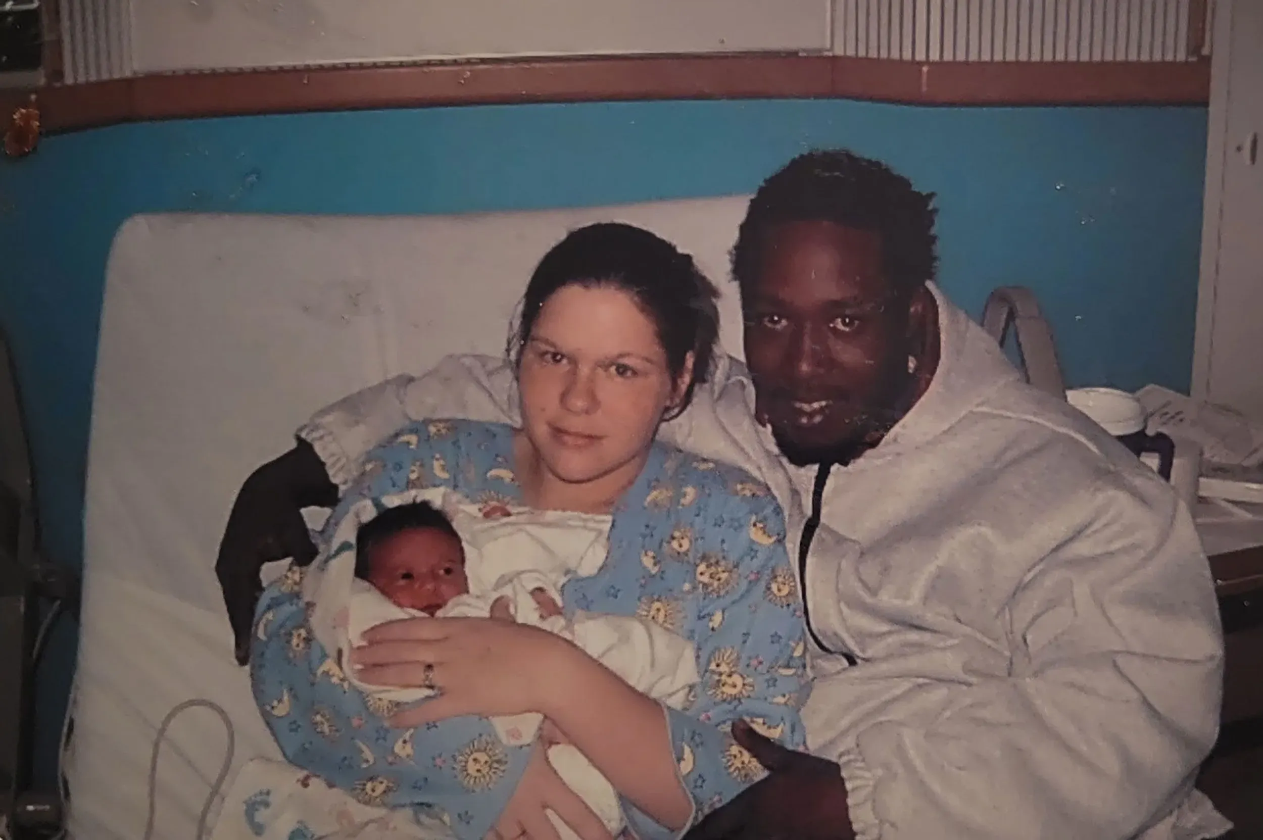 صورة عائلية تظهر كورنيليوس تايلور مع خطيبته وطفلهما حديث الولادة في المستشفى، تعكس لحظة أمل وسط التحديات.