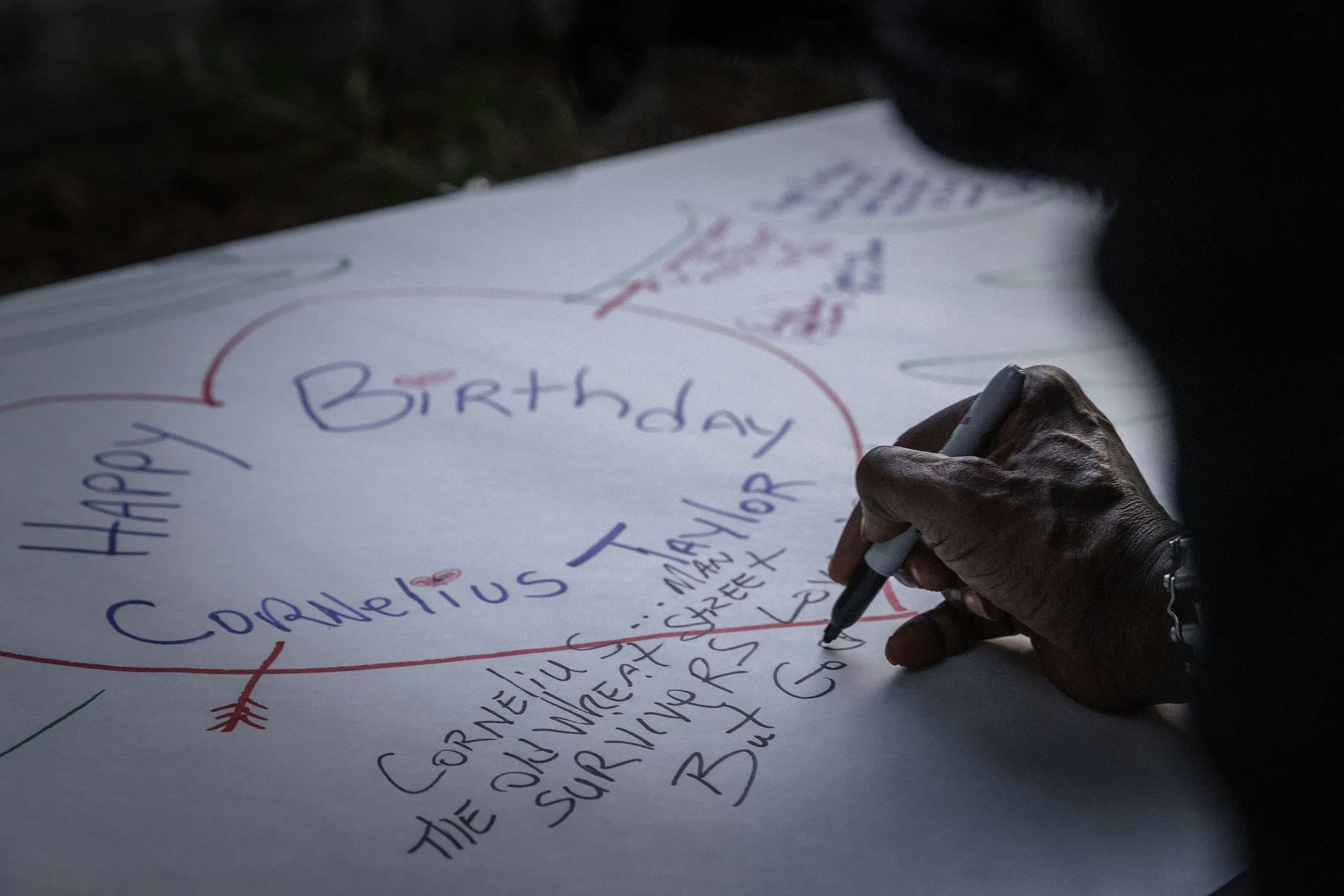 يد تكتب على لافتة كبيرة تحمل عبارة "عيد ميلاد سعيد كورنيليوس تايلور"، محاطة بقلوب ورسائل من أصدقاء وعائلة، تعبيرًا عن الذكرى.