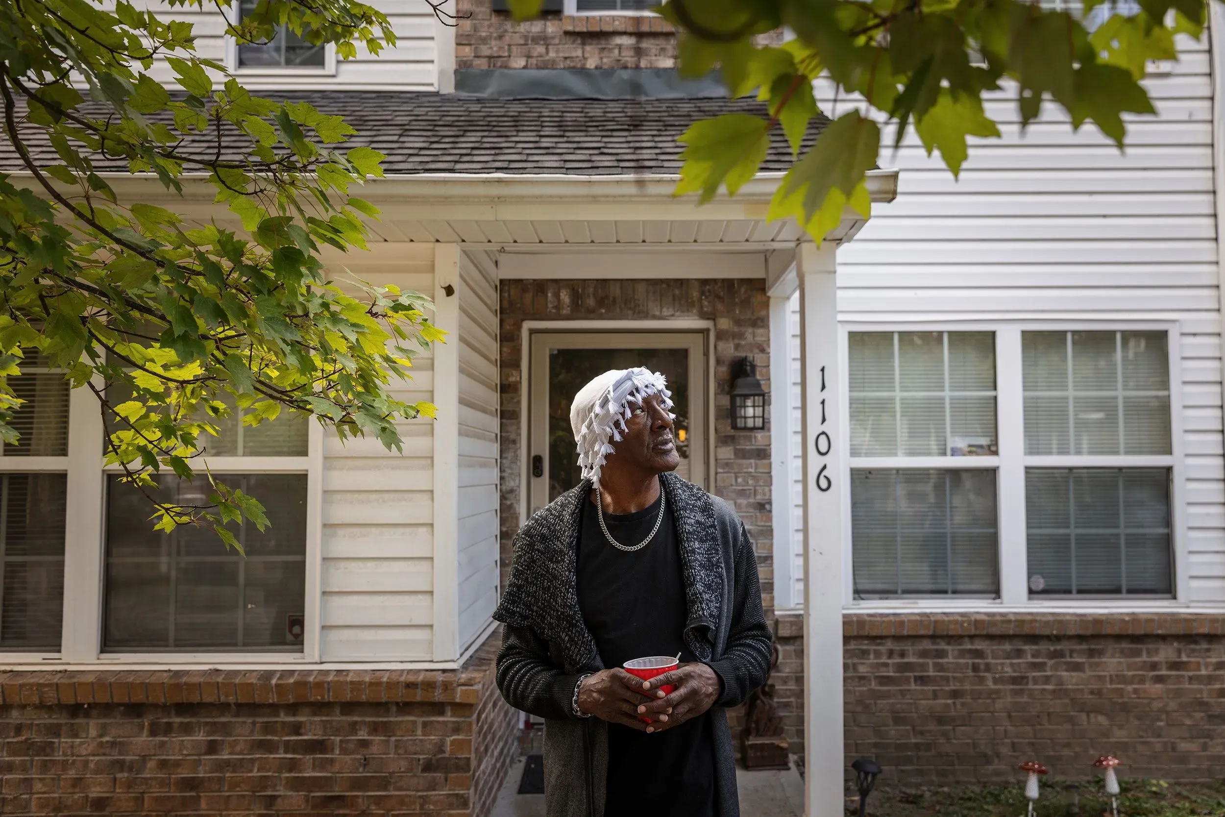 رجل يقف أمام منزله الجديد، ينظر إلى السماء بآمال جديدة، بينما يحمل كوبًا في يده. تعكس الصورة رحلة التغيير والإصلاح في حياته.