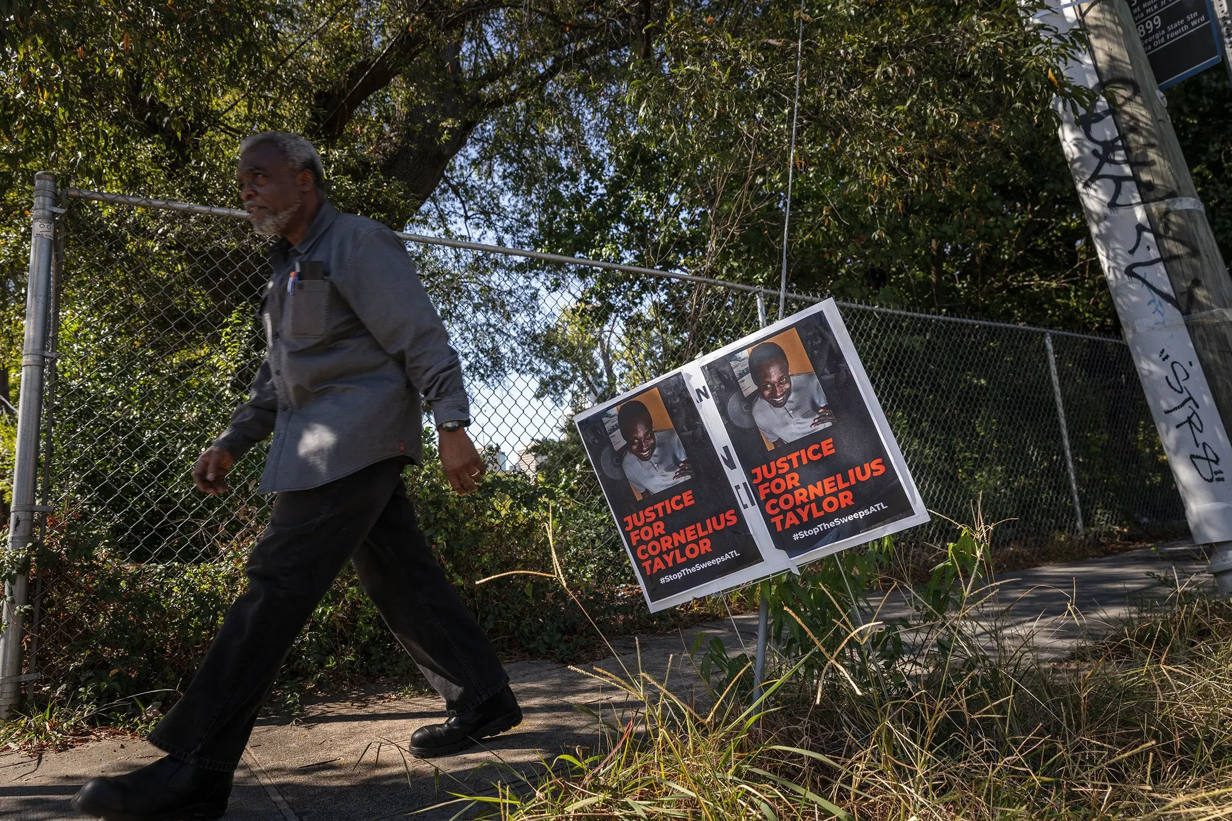 رجل مسن يسير بجوار لافتات تطالب بالعدالة لكورنيليوس تايلور، مع خلفية من الأشجار والأسوار، في أتلانتا.