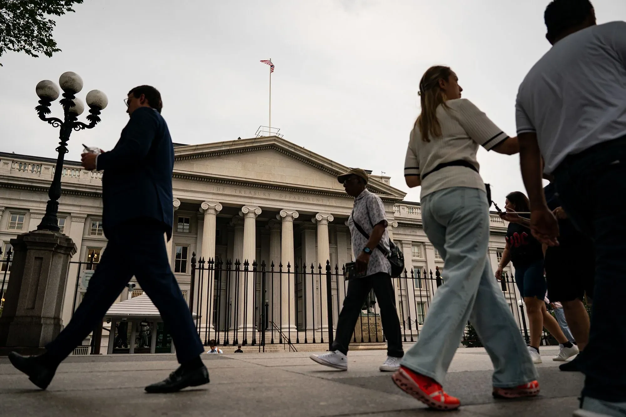 مشاة يمرون أمام مبنى وزارة الخزانة الأمريكية، مع العلم الأمريكي يرفرف في الأعلى، في سياق المخاوف الاقتصادية المتزايدة.