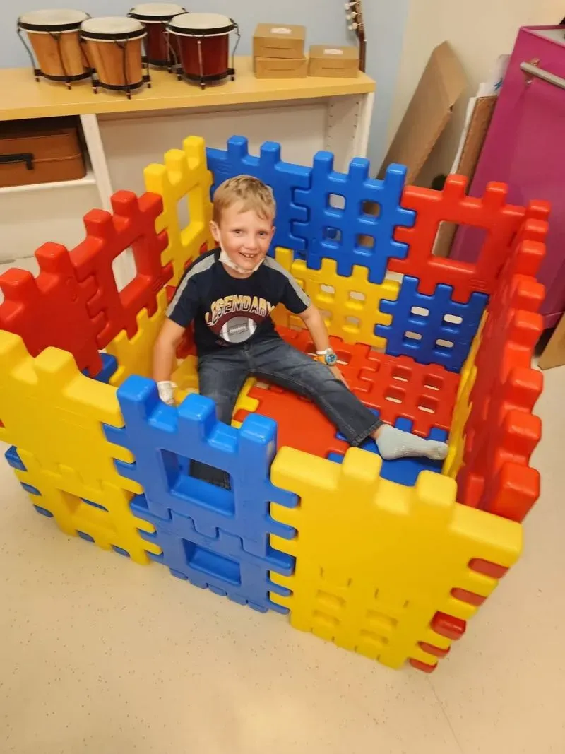 طفل صغير يجلس داخل هيكل ملون من قطع اللعب البلاستيكية في غرفة مستشفى، يعكس روح الطفولة في ظل تحديات مرض السرطان.