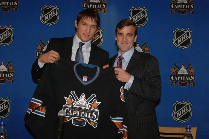 أليكس أوفيتشكين يحمل قميص واشنطن كابيتالز خلال مؤتمر صحفي، مع جورج ماكفي، بعد اختياره كأول اختيار في مسودة دوري الهوكي الوطني 2004.