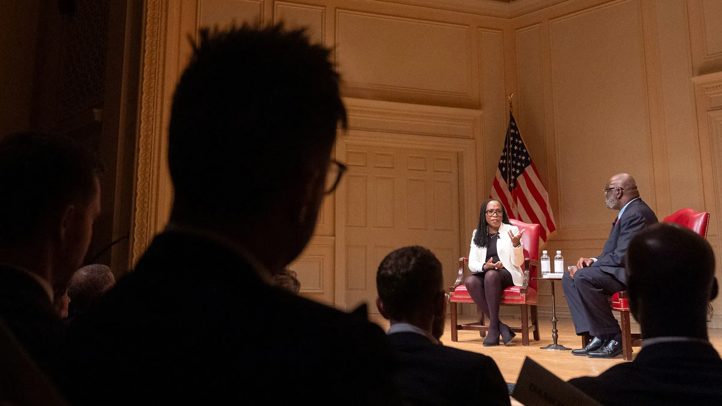 مناقشة بين القاضية كيتانجي براون جاكسون والقاضي كلارنس توماس، مع العلم الأمريكي خلفهما، في حدث عام يتناول قضايا قانونية.