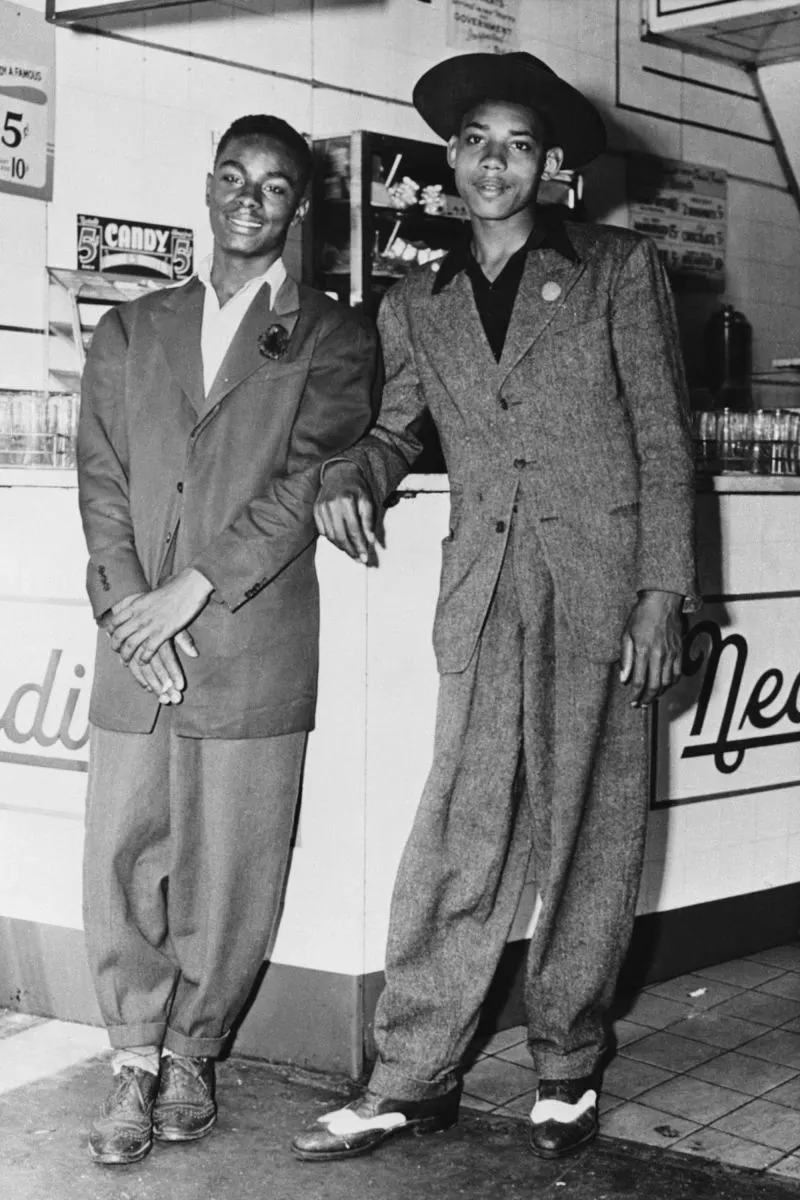 صورة تاريخية لشابين يرتديان بدلات أنيقة، تعكس أسلوب الدانديزم في عصر نهضة هارلم، مع تفاصيل دقيقة حول الموضة السوداء.