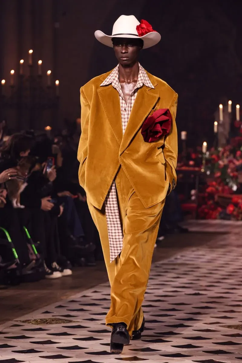 عارض أزياء يرتدي بدلة زوت باللون البرتقالي الداكن وقبعة بيضاء، مع لمسة من الأناقة العصرية، في عرض أزياء يبرز تأثير الموضة السوداء.