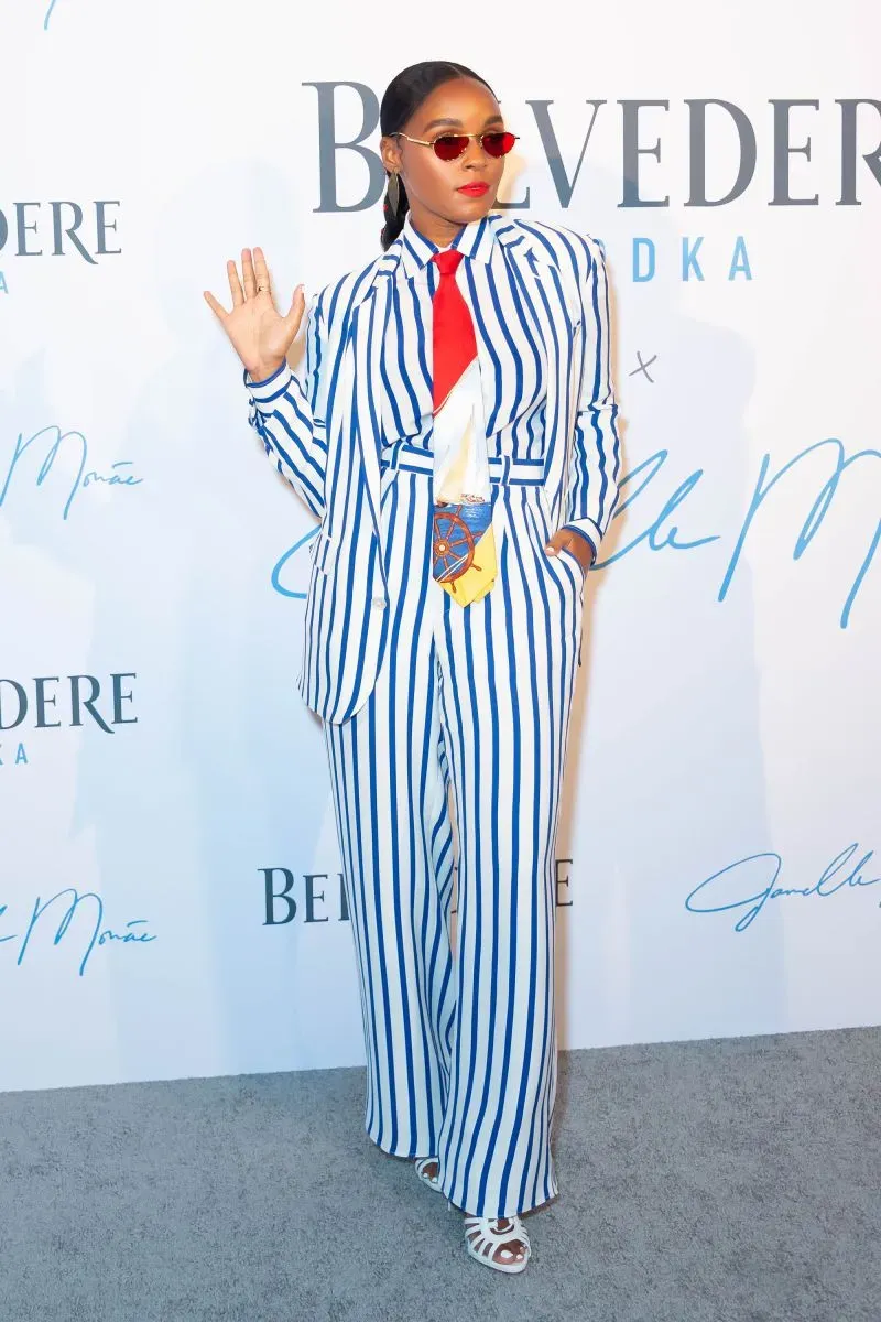 امرأة ترتدي بدلة مخططة بالأبيض والأزرق مع ربطة عنق حمراء ونظارات شمسية، تعبر عن أسلوب الدانديزم في الموضة.