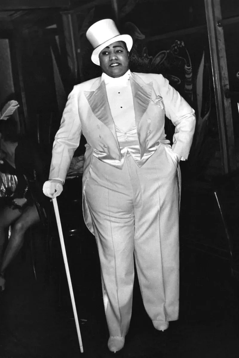 شخص يرتدي بدلة زوت بيضاء وقبعة علوية، مع عصا، يعبر عن أناقة عصر النهضة في هارلم وتأثيره على الموضة السوداء.
