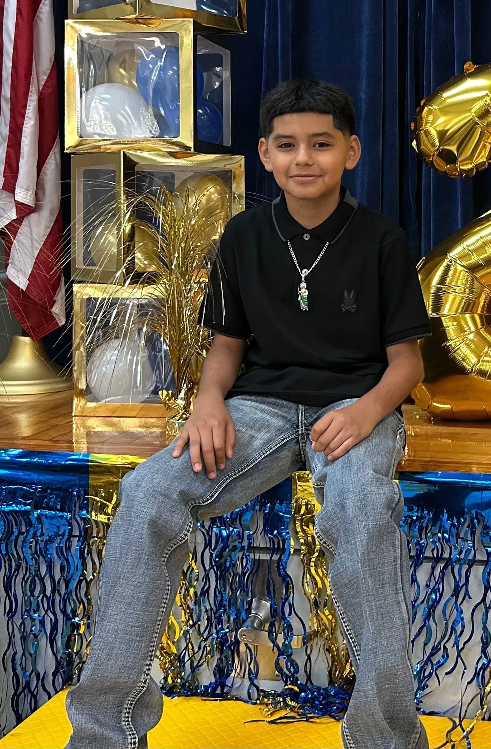 طفل يبلغ من العمر 11 عامًا يجلس مبتسمًا في حفل، محاط ببالونات وزينة، يمثل ضحية حادث مأساوي أثناء لعب مقلب مع ابن عمه.