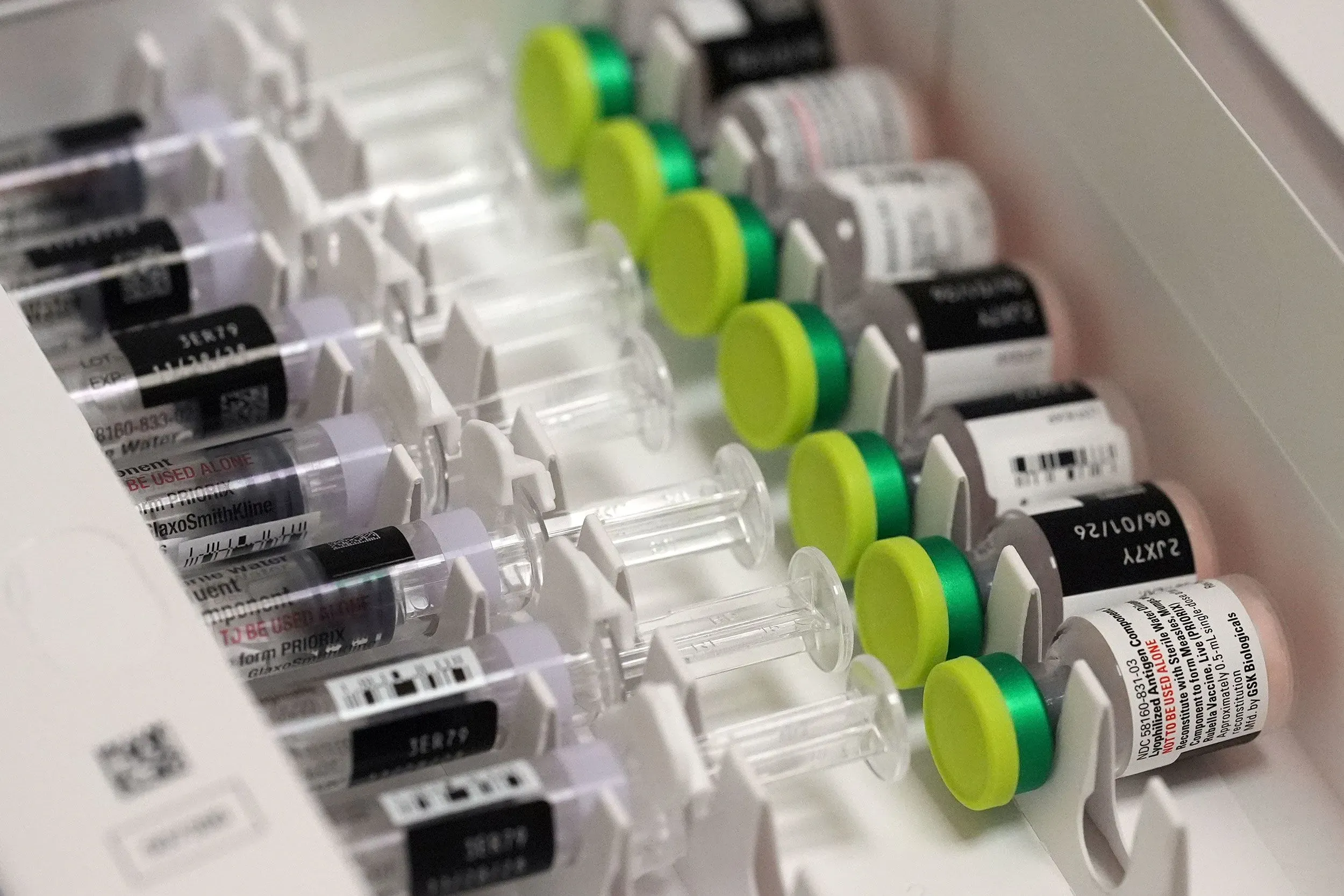 عبوات لقاح الحصبة مرتبة في علبة، مع محاقن جاهزة للاستخدام، تعكس جهود مكافحة تفشي الحصبة في المجتمع.