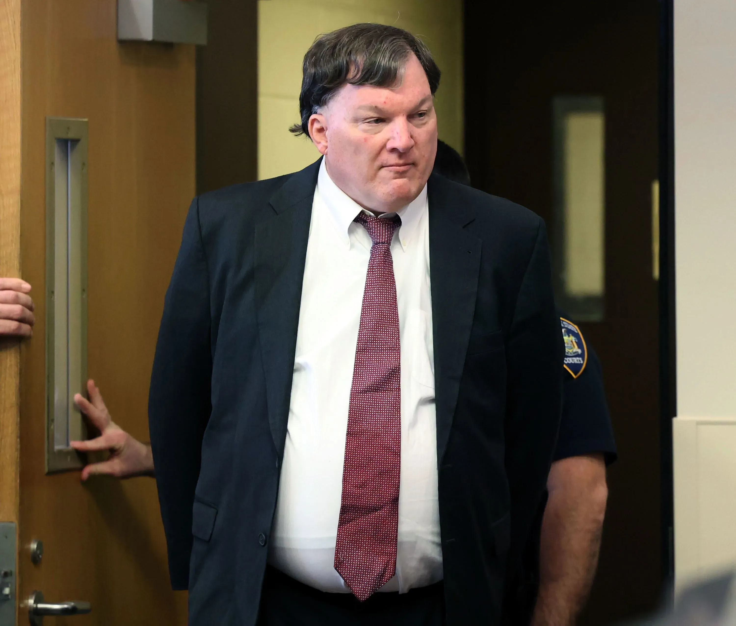 رجل يرتدي بدلة رسمية يدخل قاعة المحكمة، حيث يُتوقع أن تُناقش أدلة الحمض النووي في قضية قتل متهم بها.