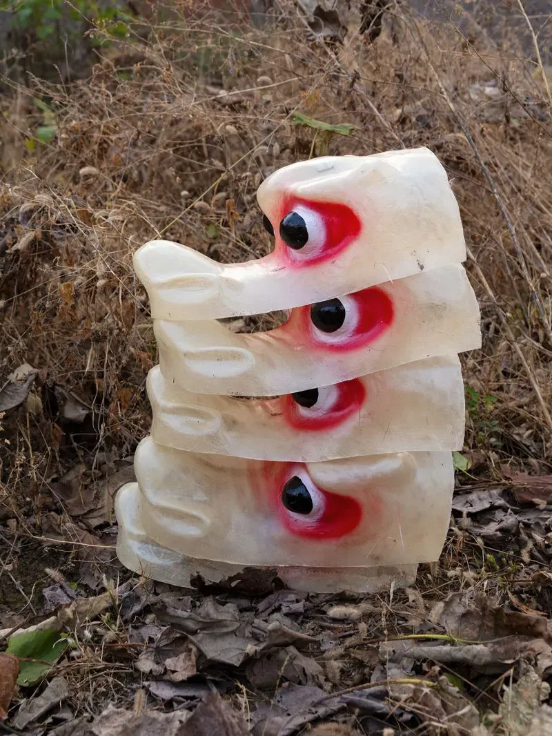 أقنعة ملونة تُظهر عيونًا حمراء وسوداء، موضوعة فوق بعضها في منطقة زراعية جافة، تعكس تراث مهرجان شيهوو التقليدي في الصين.