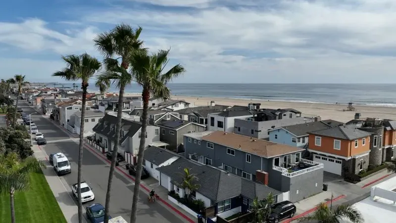 منظر بانورامي لشاطئ نيوبورت بيتش في كاليفورنيا، يظهر المنازل والشوارع القريبة من البحر، مع أشجار النخيل تحت سماء زرقاء.