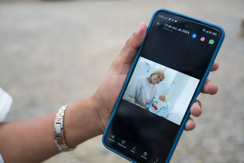 امرأة تحمل هاتفًا ذكيًا تعرض صورة لها مع طفلها في المستشفى، تعكس التحديات التي تواجهها بعد الإفراج عنها بموجب قانون المنفعة العامة في كولومبيا.