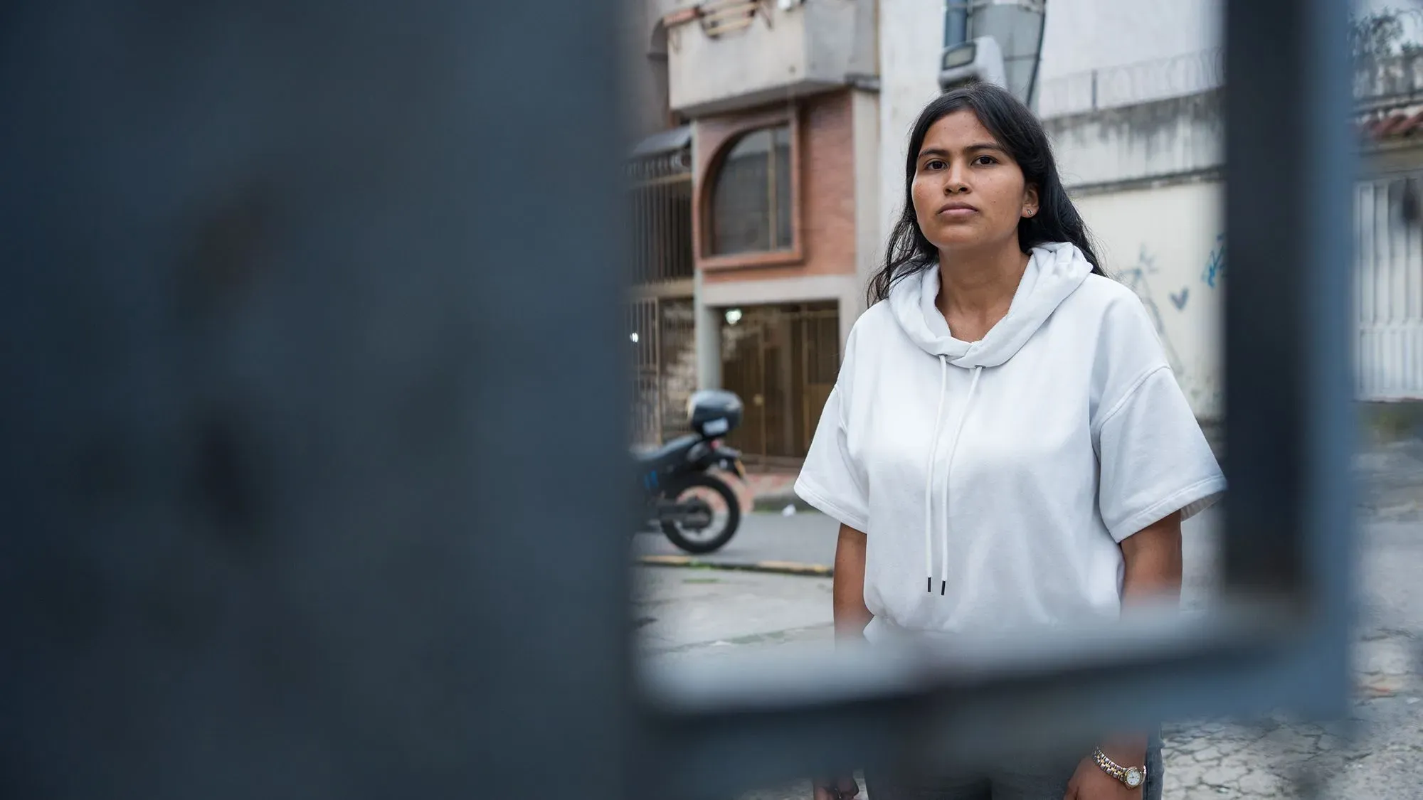 امرأة شابة ترتدي سترة بيضاء، تنظر بجدية نحو الكاميرا في حي حضري، تعكس تحديات إعادة الاندماج بعد الإفراج عنهن من السجن.