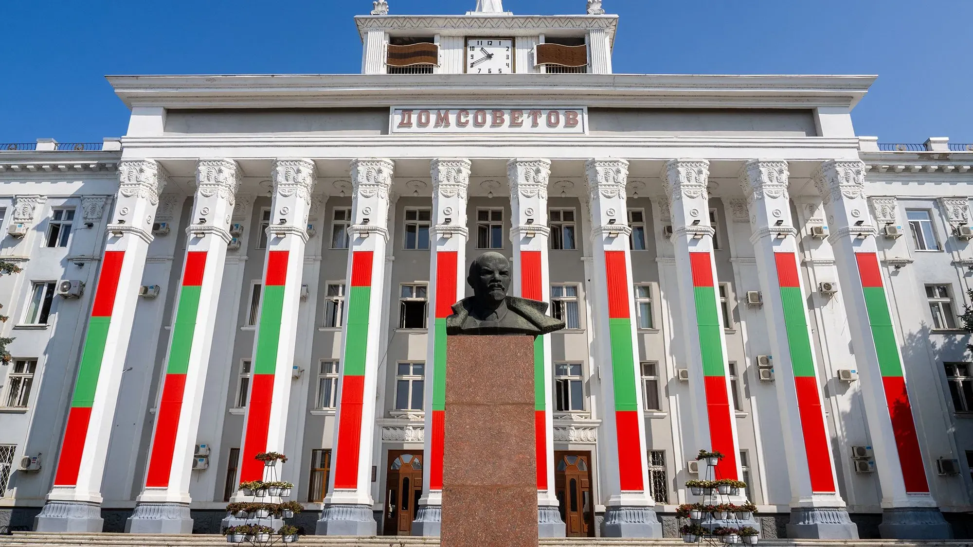 واجهة مبنى حكومي في ترانسنيستريا مزينة بألوان العلم الوطني، مع تمثال نصفي لشخصية تاريخية أمامه، تحت سماء زرقاء.