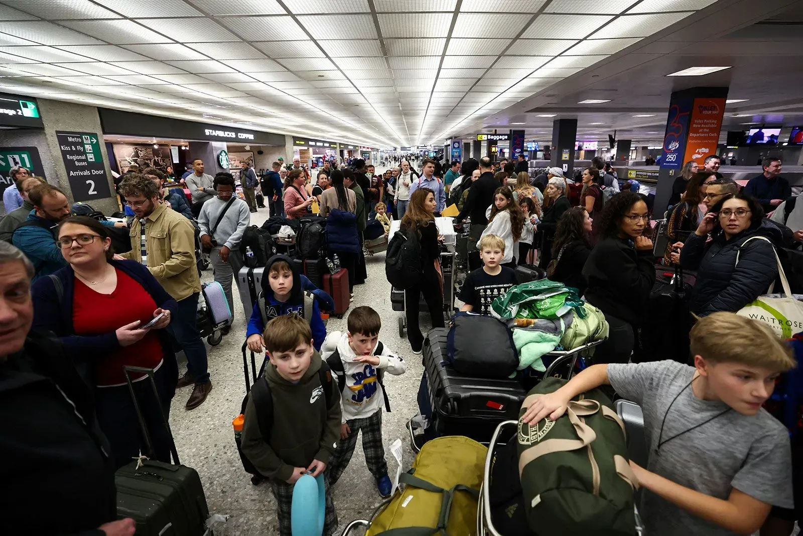 ازدحام كبير في مطار مزدحم، حيث يظهر المسافرون مع حقائبهم، بما في ذلك عائلات وأطفال، في انتظار الرحلات وسط حالة من الفوضى.
