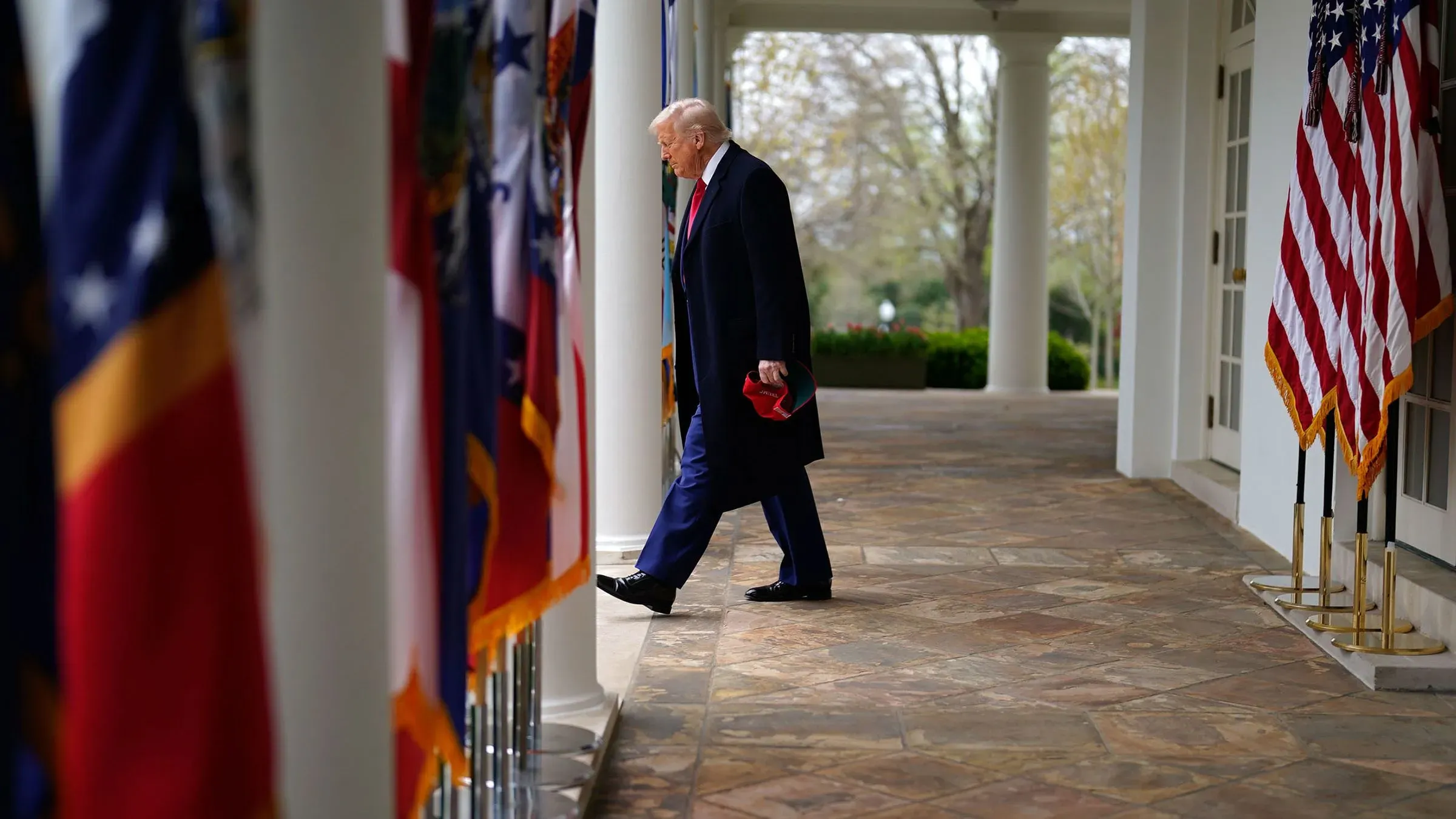 ترامب يسير في ممر البيت الأبيض بين أعلام الولايات، معبرًا عن تحدياته القضائية وسياساته المثيرة للجدل.
