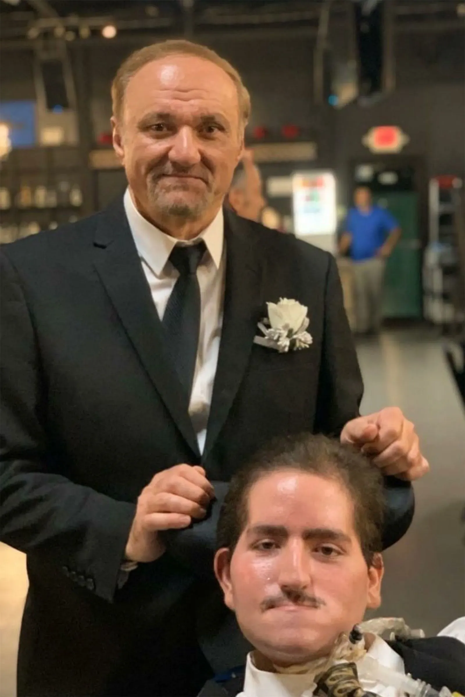 صورة تظهر والد وائل طرابيشي، ماهر، في بدلة رسمية، وهو يقف خلف ابنه المعاق جسديًا، الذي يجلس على كرسي متحرك، في لحظة مؤثرة تعكس العلاقة العائلية.